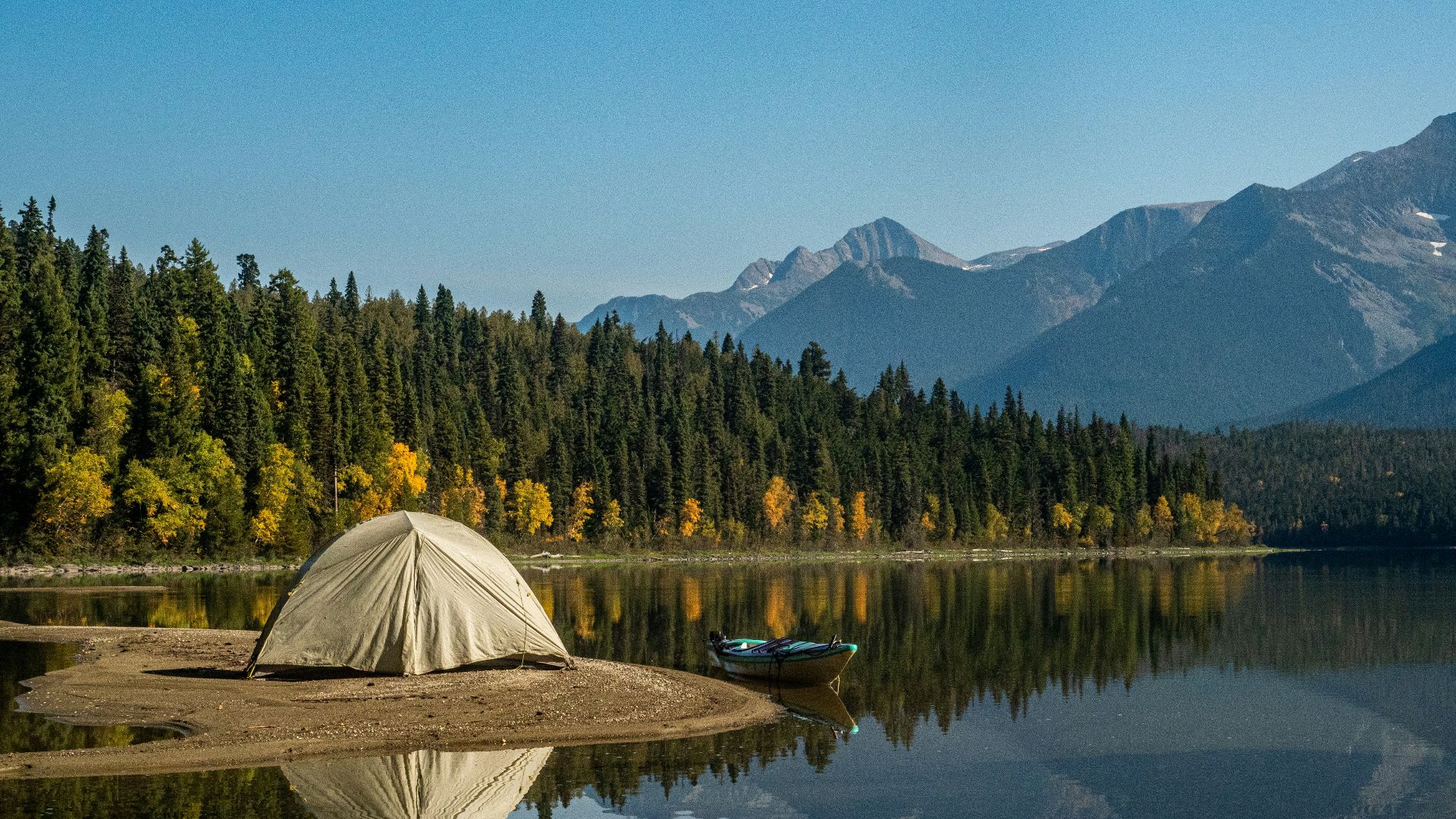 white tent on lake near green trees and mountain under blue sky during daytime