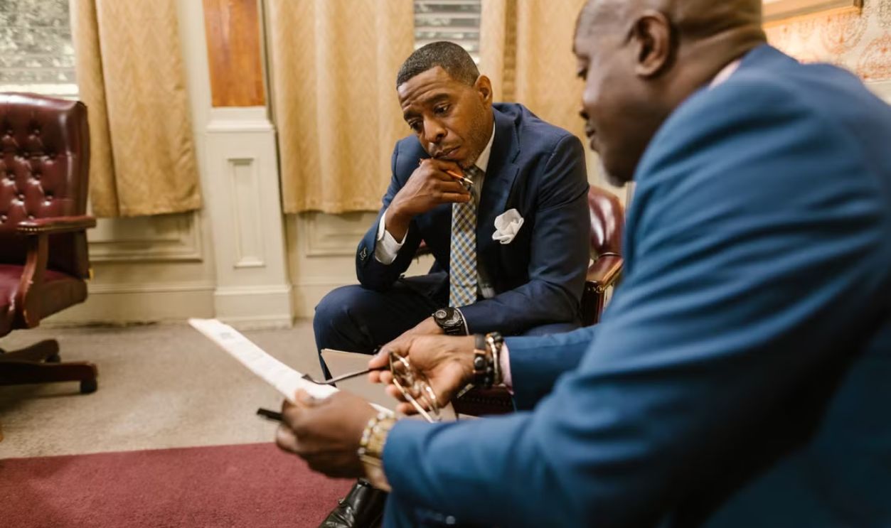 Two executives in business attire discuss documents in an office setting