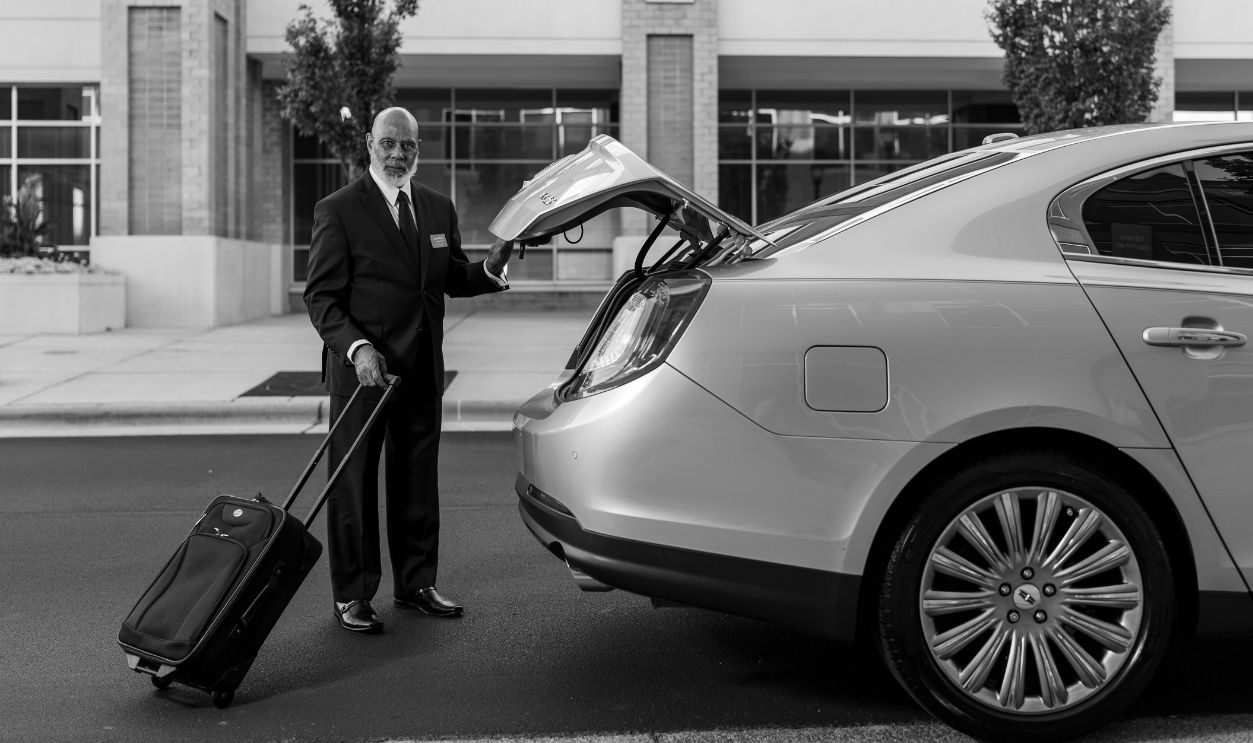 Chauffeur in suit loading luggage into luxury car trunk outside a modern building