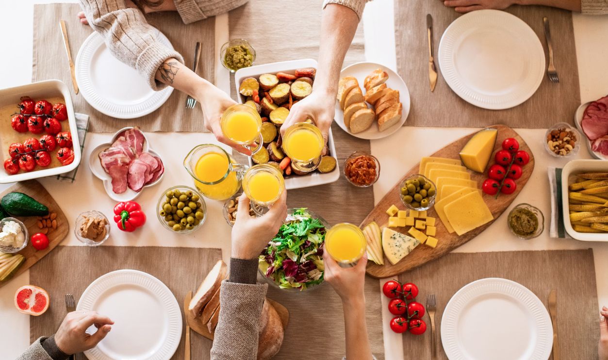 Top view of a family toasting at a lunch table with cheese, olives, and fresh salads