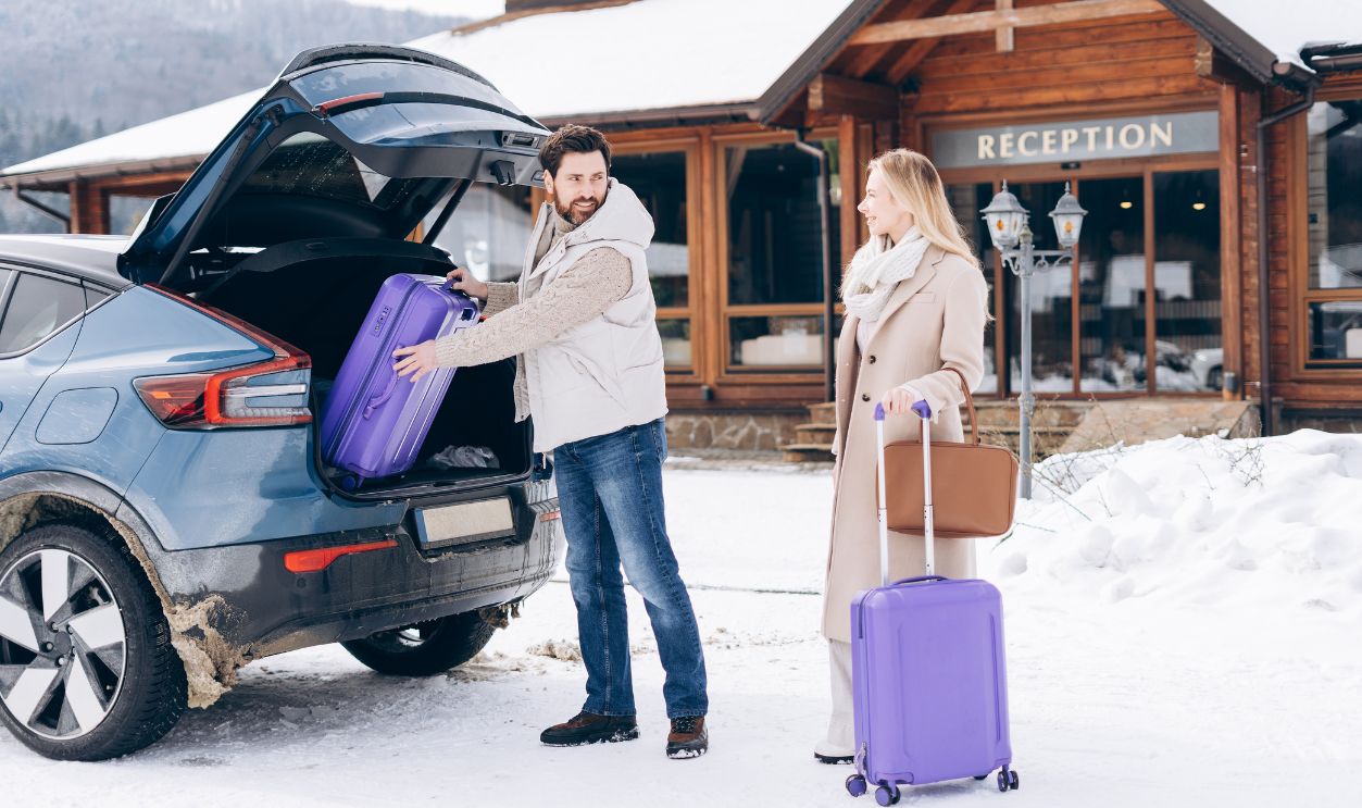 Smiling happy couple having car trip holding suitcases staying in modern hotel in mountains. Active lifestyle, weekend concept