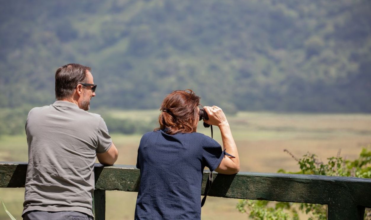 A couple relaxing outdoors, using binoculars to enjoy a scenic landscape view.
