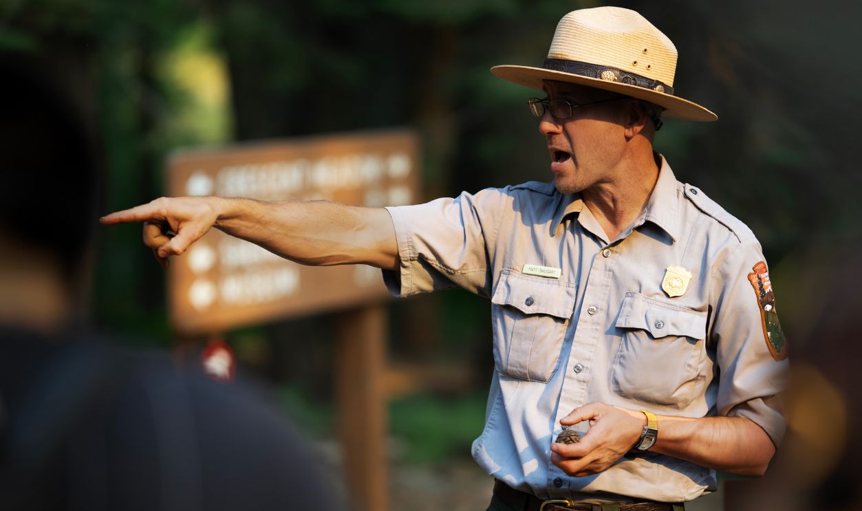 Park ranger guiding a group through a forest area, pointing with emphasis.