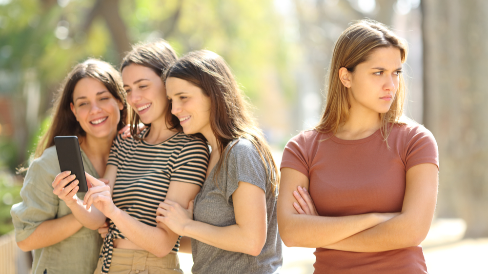 Angry woman being ignored by her happy friends who are checking smart phone