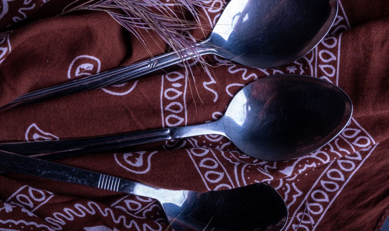 Three metal spoons on patterned brown fabric create a vintage still life look