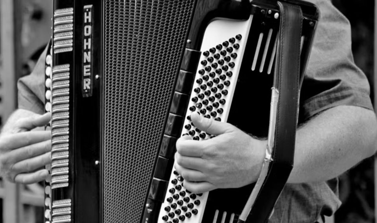 A black and white photo of a street musician playing an accordion, showcasing the instrument and musician's hands