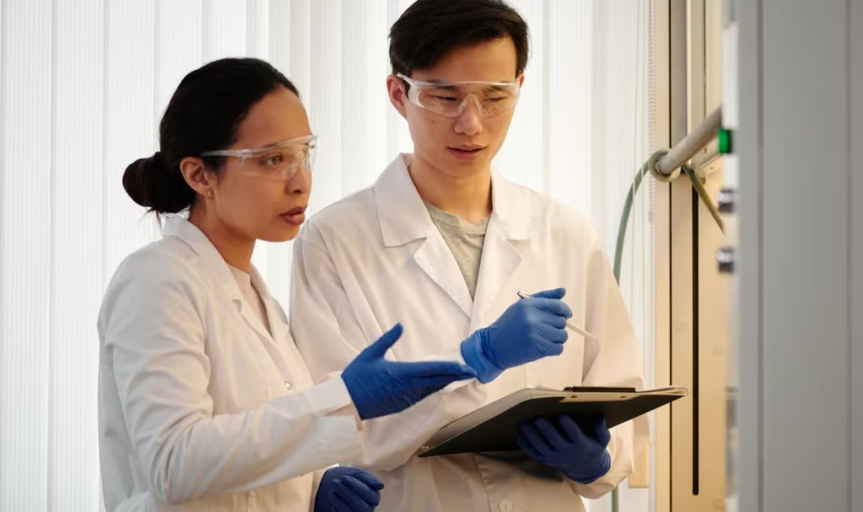 Researchers discussing data in a laboratory setting, wearing safety gear and blue gloves