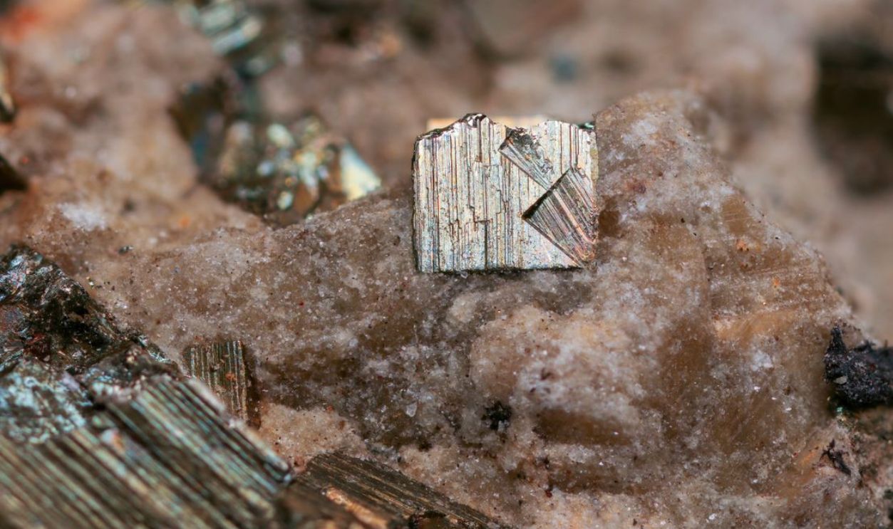 Detailed close-up of pyrite crystal on rocky surface, showcasing natural textures and colors