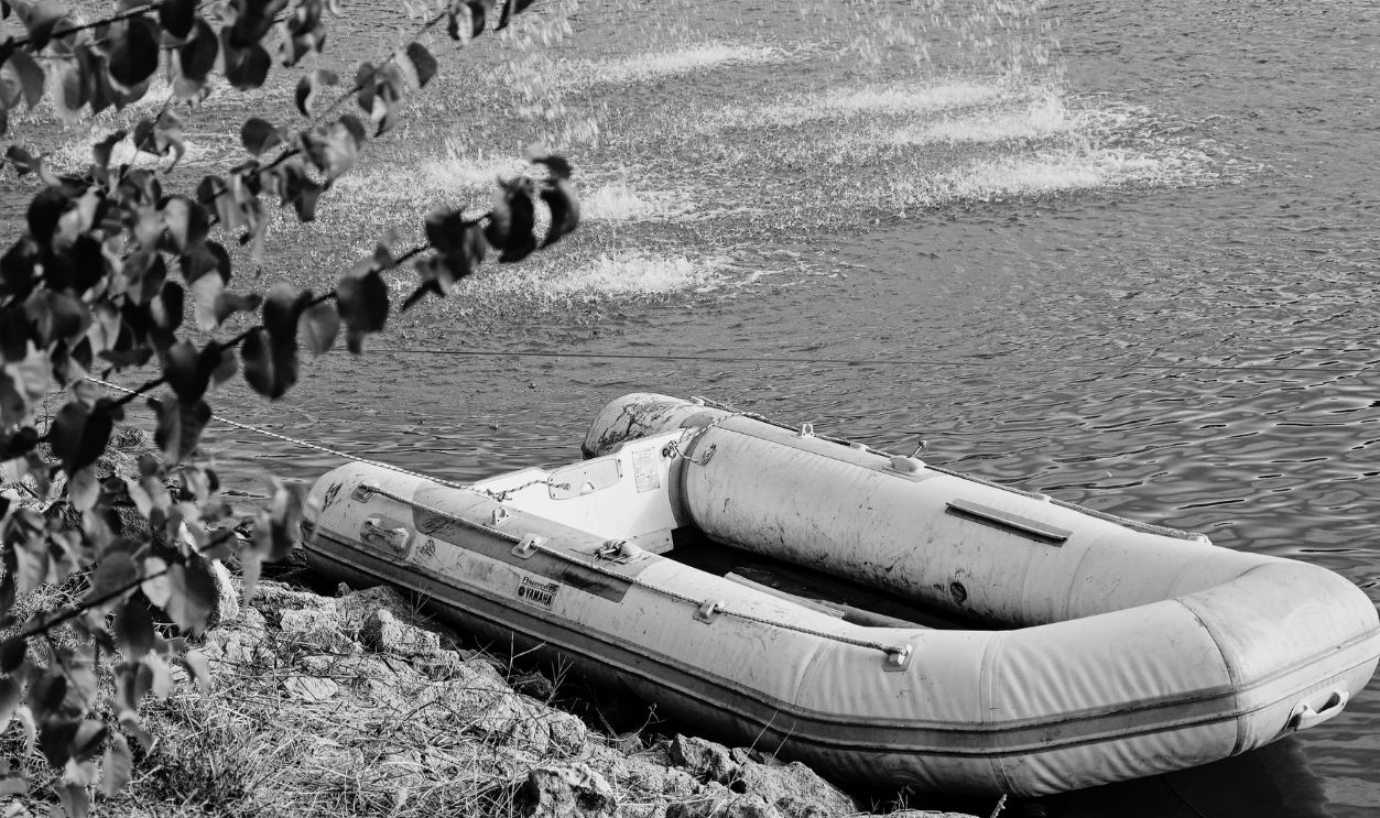 A solitary inflatable boat moored by a serene lake with rippling waters and nearby foliage