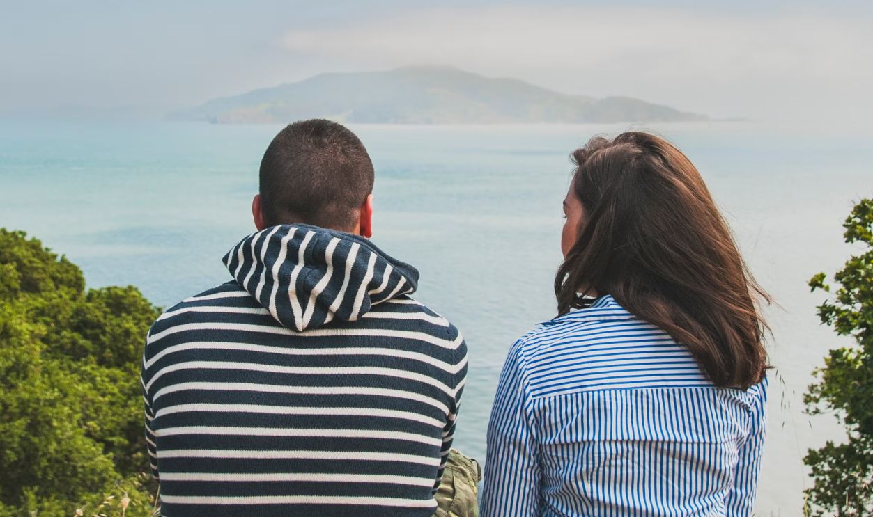 A couple sitting outdoors enjoying a scenic ocean view under a bright sky.