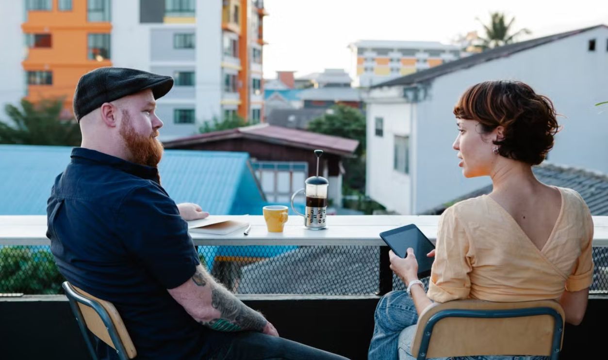 A couple enjoying conversation and coffee outdoors on a city terrace during the day.