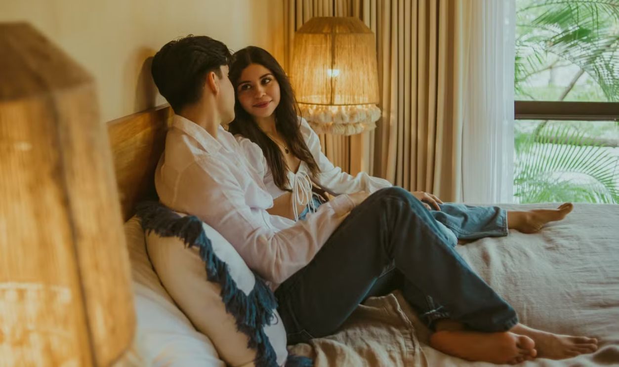Romantic couple enjoying a cozy moment in a warmly lit bedroom.