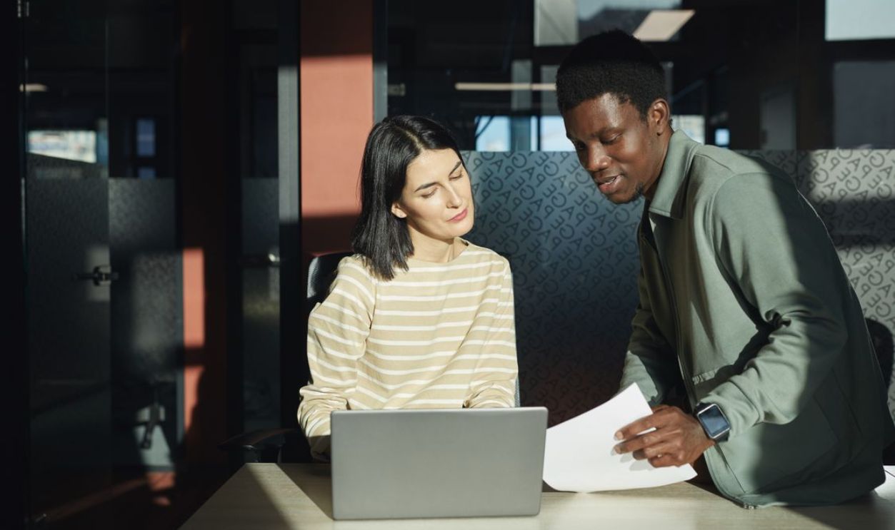 Two professionals discussing work over a laptop in a bright, modern office setting.