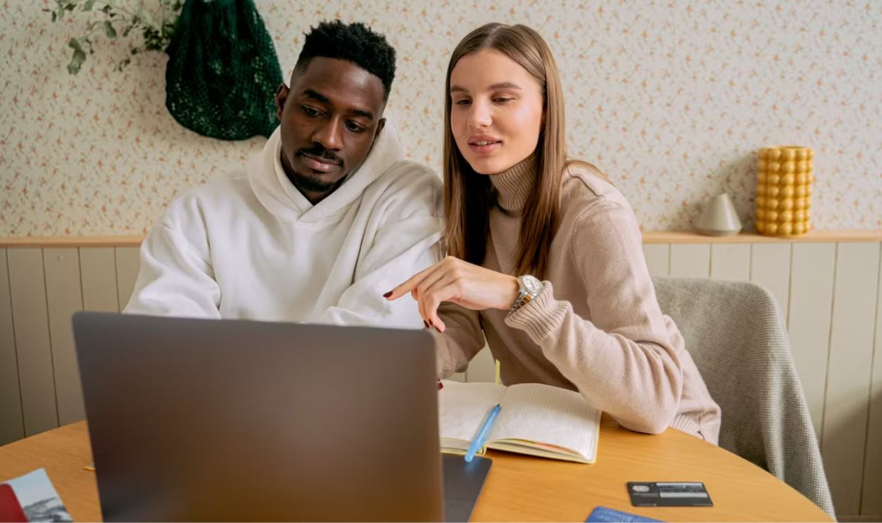 An interracial couple engaged in collaborative work on a laptop indoors, fostering teamwork.
