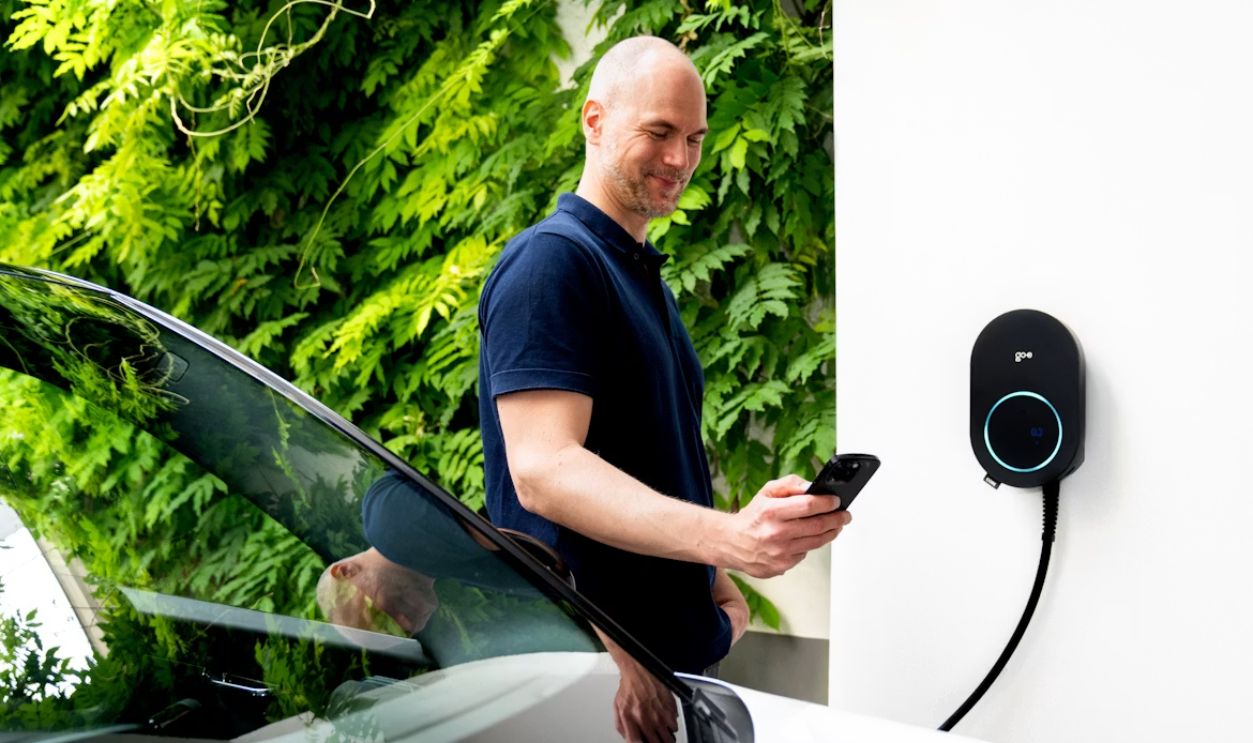 Man checks phone while charging his EV with the go-e Charger CORE