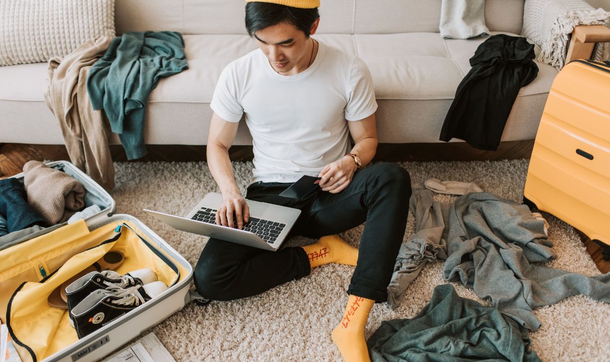 Man multitasking by packing luggage while working on a laptop
