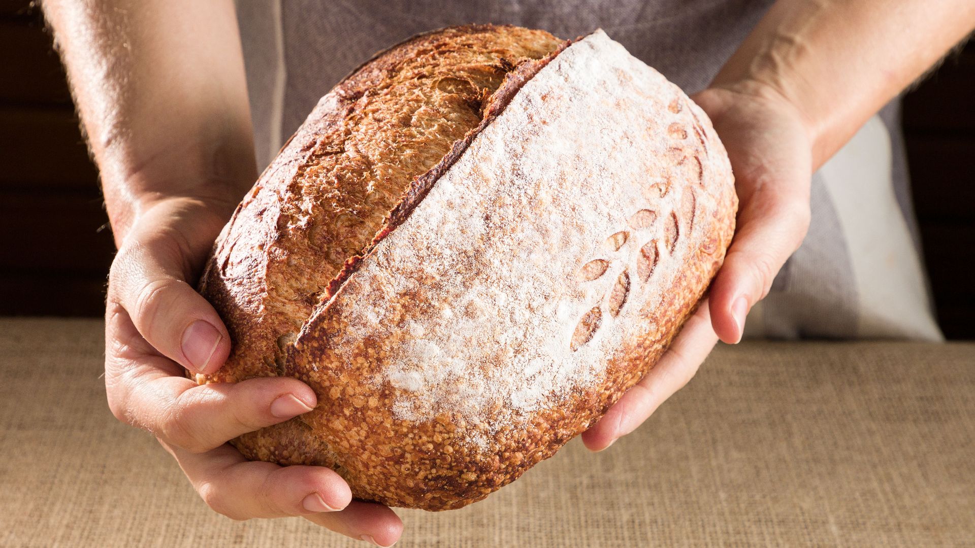 Close-up of artisan bread held by hands against a burlap background, emphasizing freshness and quality.