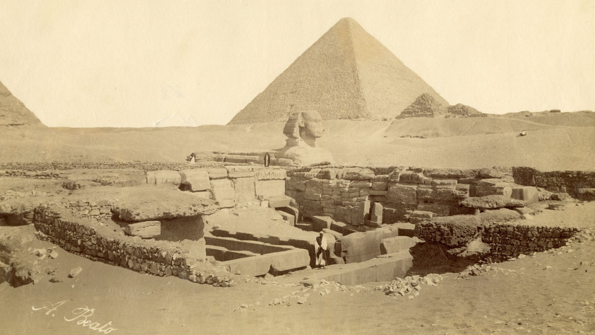 The photograph shows an overview of the monuments in the Giza Plateau, in particular the Pyramid of Khufu with satellite pyramids (in the background), the Valley Temple of Khafre (in the foreground) where part of the pyramid can also be seen on the left, 