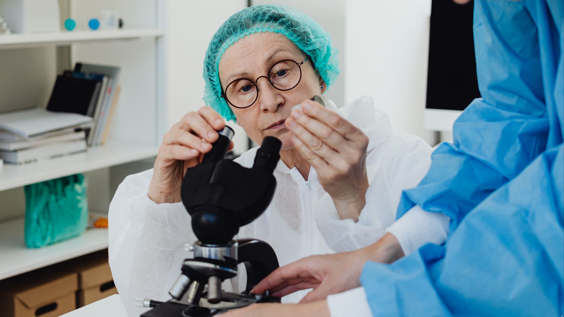 Researchers using microscope in a medical lab setting, equipped with protective gear and scientific tools.