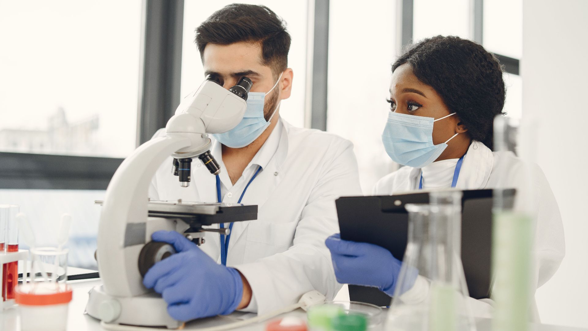 Researchers using a microscope and taking notes in a modern lab.