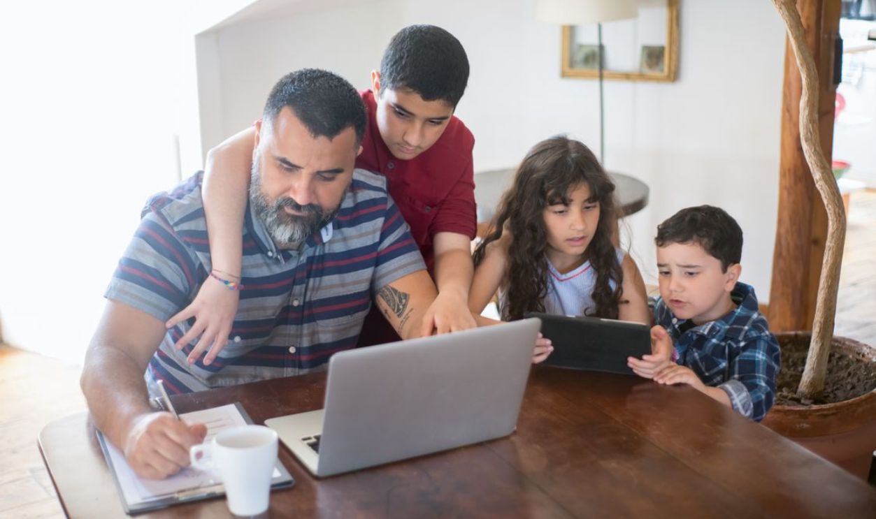 A father and his children engaged in activities with a laptop and tablet at home.