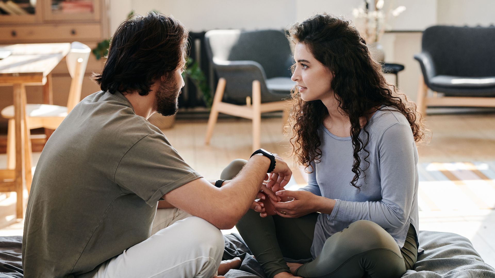 A couple sitting closely on a bed, engaged in a thoughtful discussion in a cozy home setting.