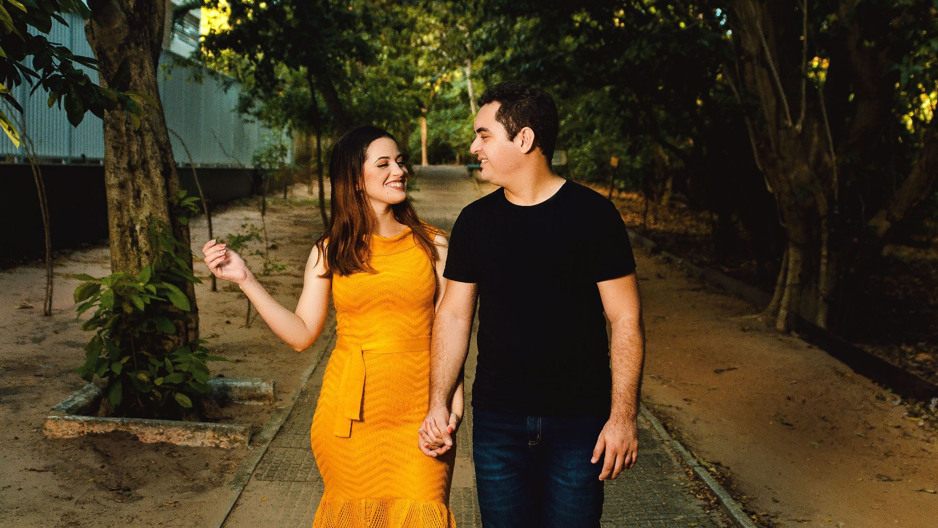 Couple walking hand in hand in a sunlit park, smiling and enjoying each other's company.