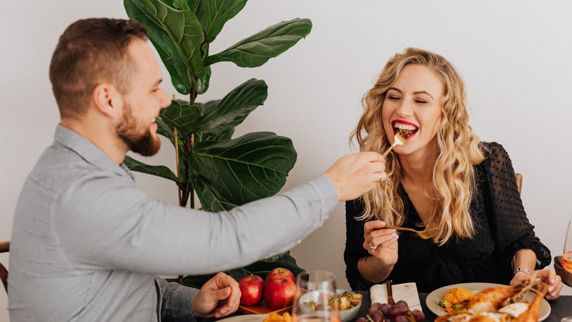 A joyful couple shares a festive meal with roasted chicken and wine, enjoying each other's company.