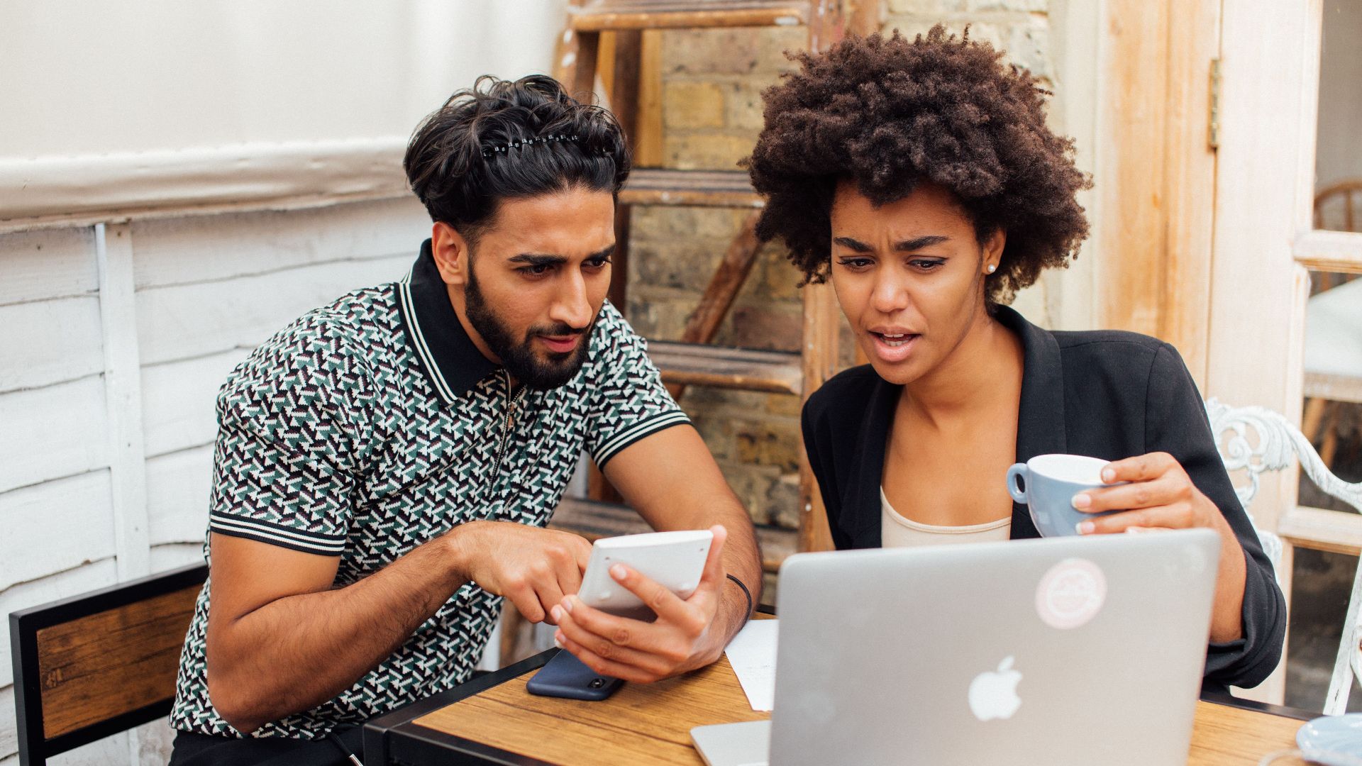Two young professionals working together on a laptop and phone at a cafe.