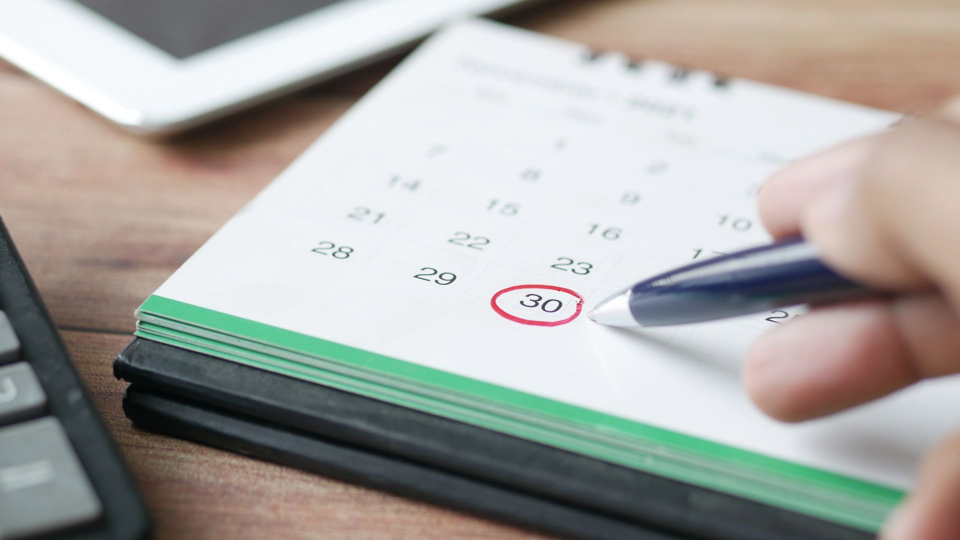 Close-up shot of a hand marking a date on a calendar with a pen, emphasizing planning and scheduling.
