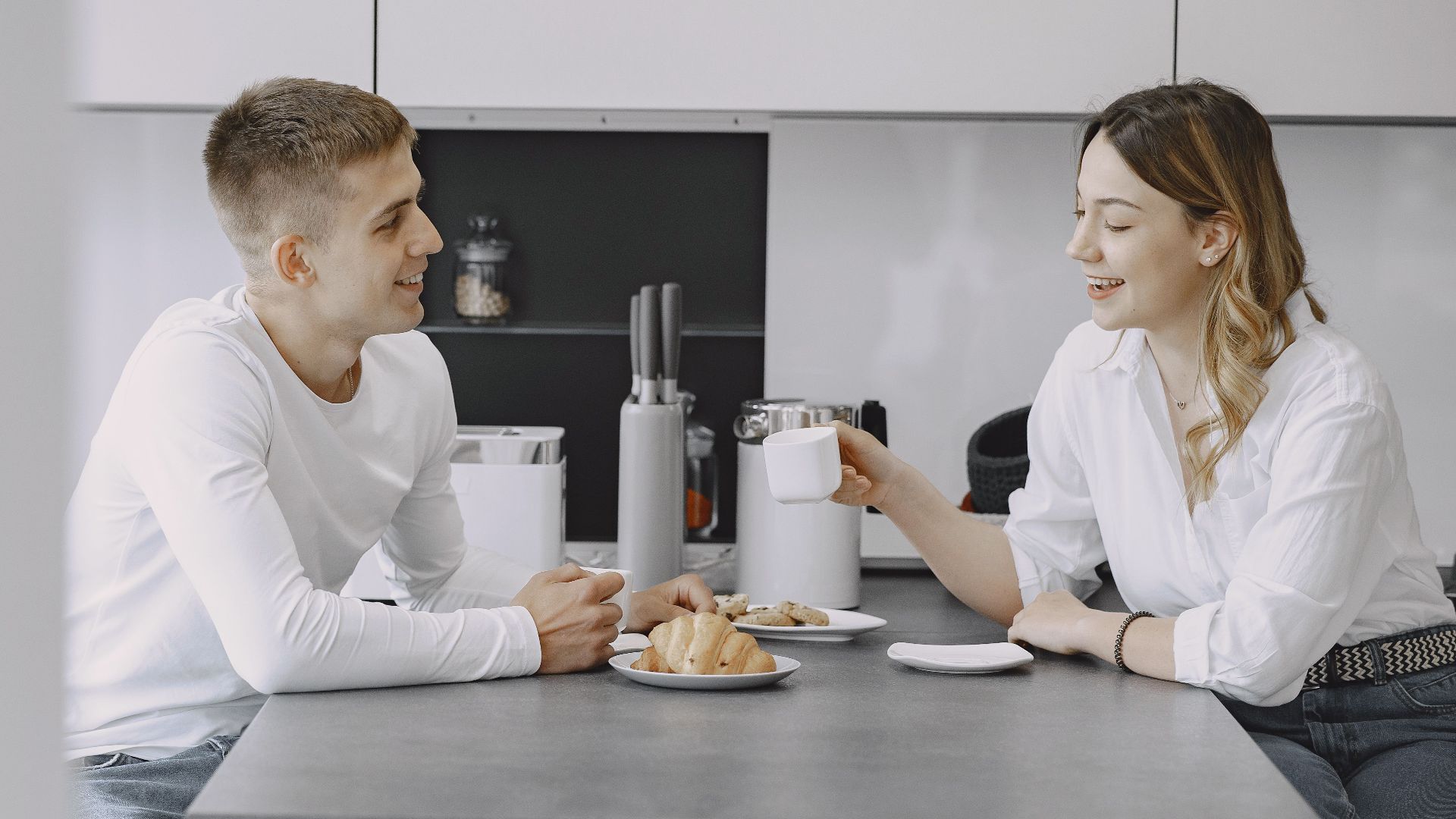 Happy couple conversing over breakfast in a modern kitchen, enjoying coffee and pastries.