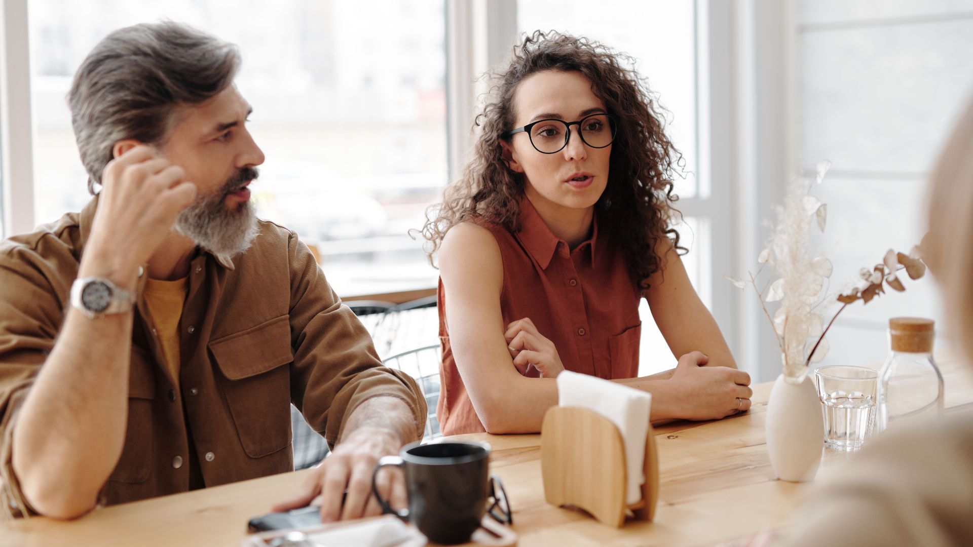 Adults in conversation at a coffee shop sharing ideas and companionship.
