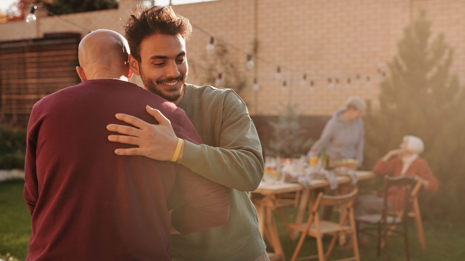 Two men hugging at a lively outdoor gathering with family and friends.
