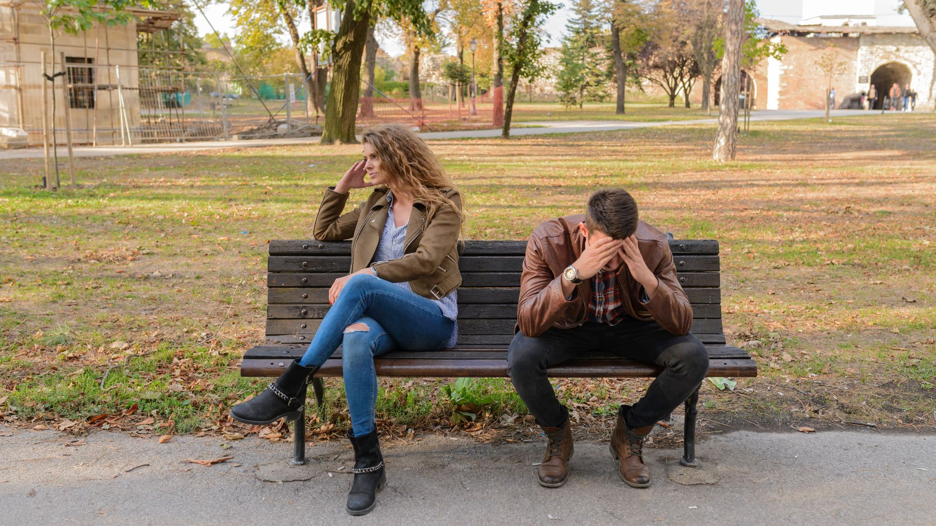 An upset couple seated on a park bench, expressing frustration during an autumn day.