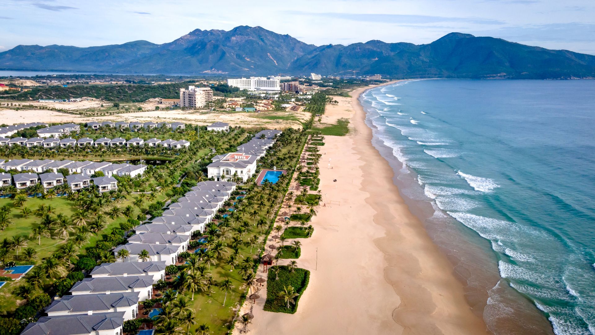 A stunning aerial view of beachfront resorts, sandy shores and blue ocean waves.