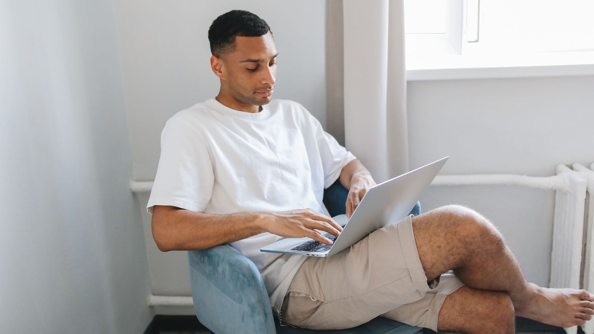 Young man focused on typing on a laptop while sitting in a comfortable chair.