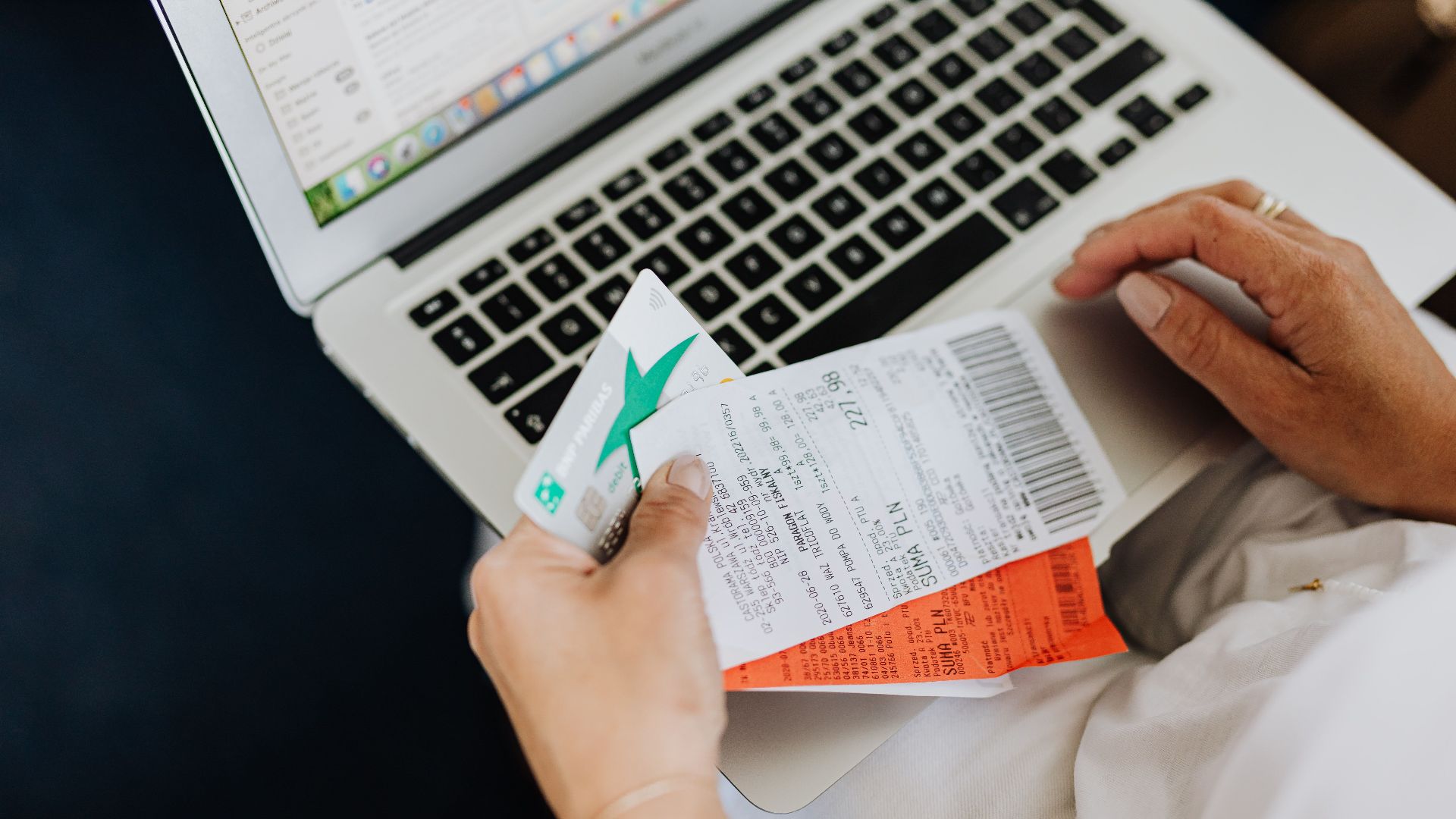 Close-up of hands holding receipts and a bank card in front of a laptop, representing online shopping and e-commerce.