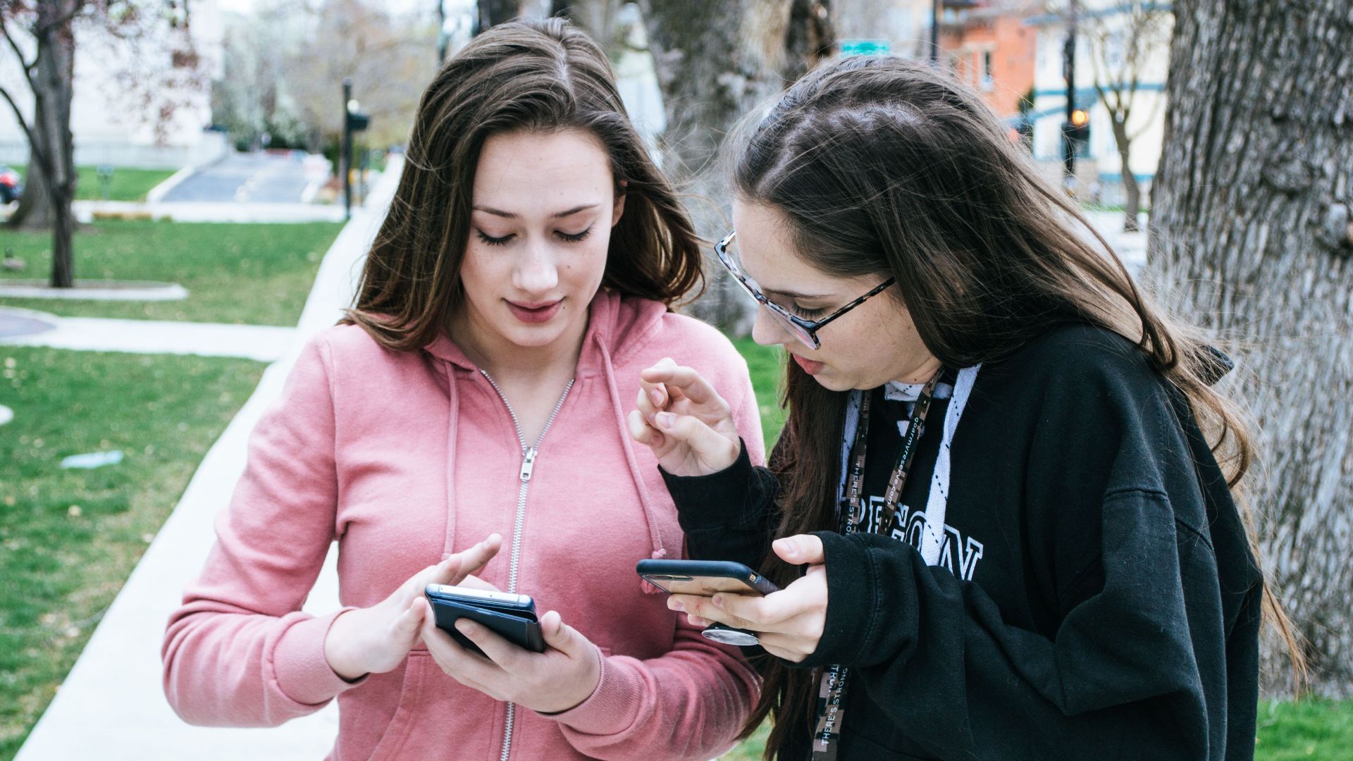 Two young women using smartphones outdoors, sharing information.