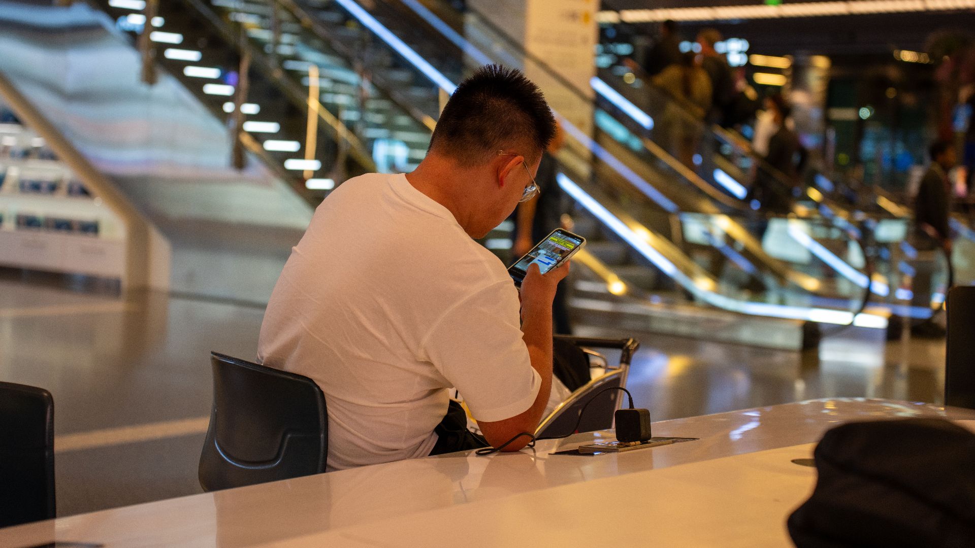 Adult using smartphone in modern airport terminal, Doha, Qatar. Busy travel scene with escalator.