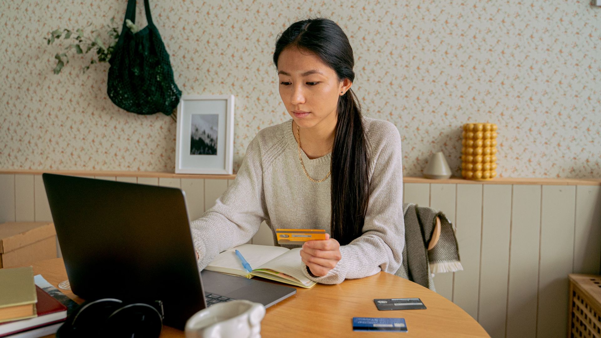 A woman using a laptop and credit card for online shopping at a cozy indoor setting.