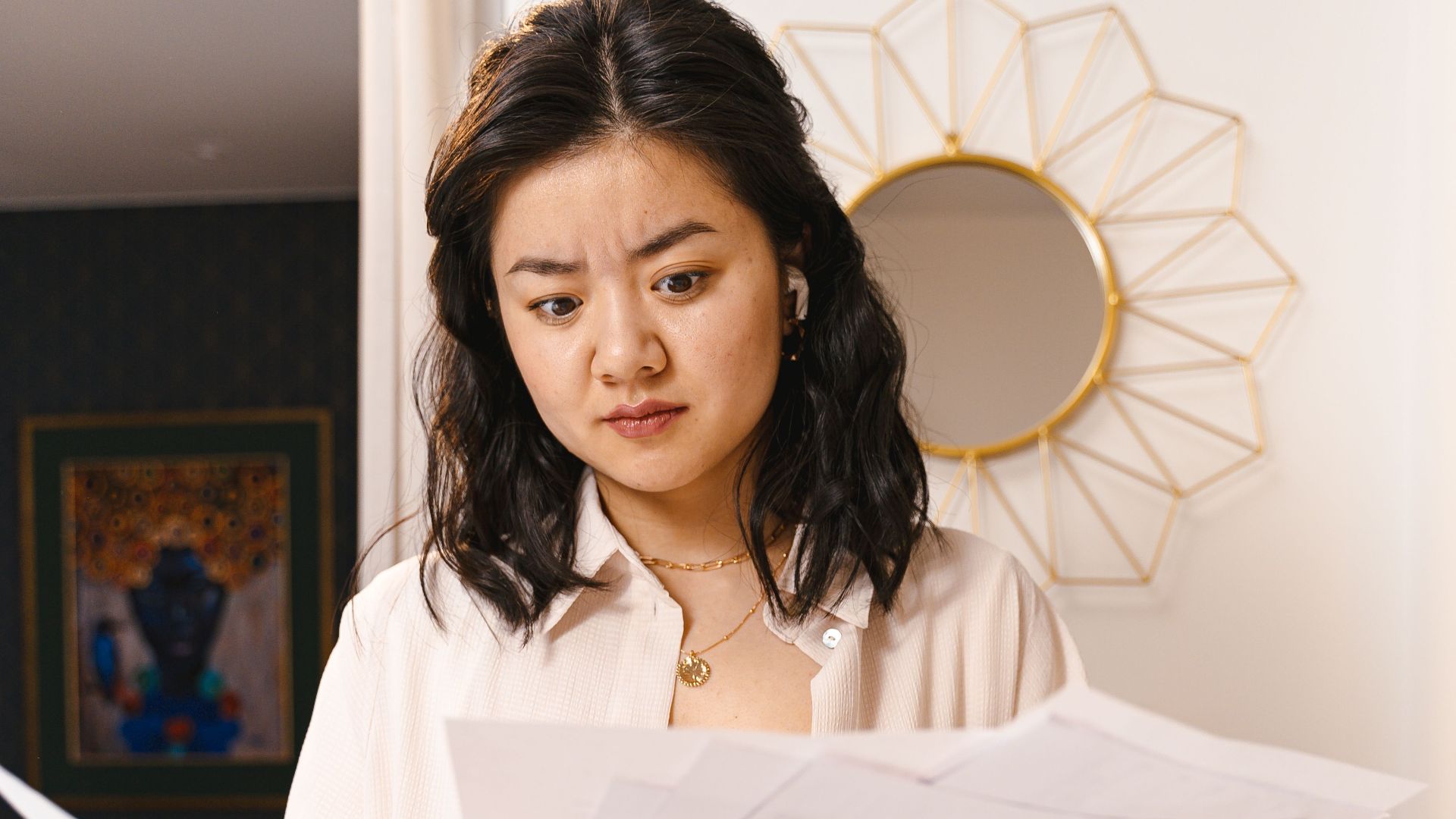 Young woman looks confused while reviewing documents in a modern home interior.