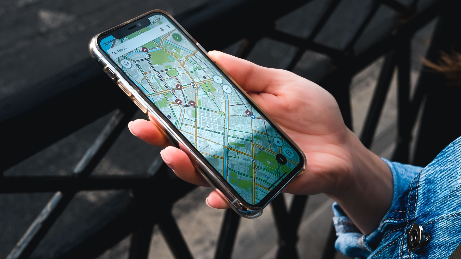 An outdoor close-up of a hand holding a smartphone displaying a map application.