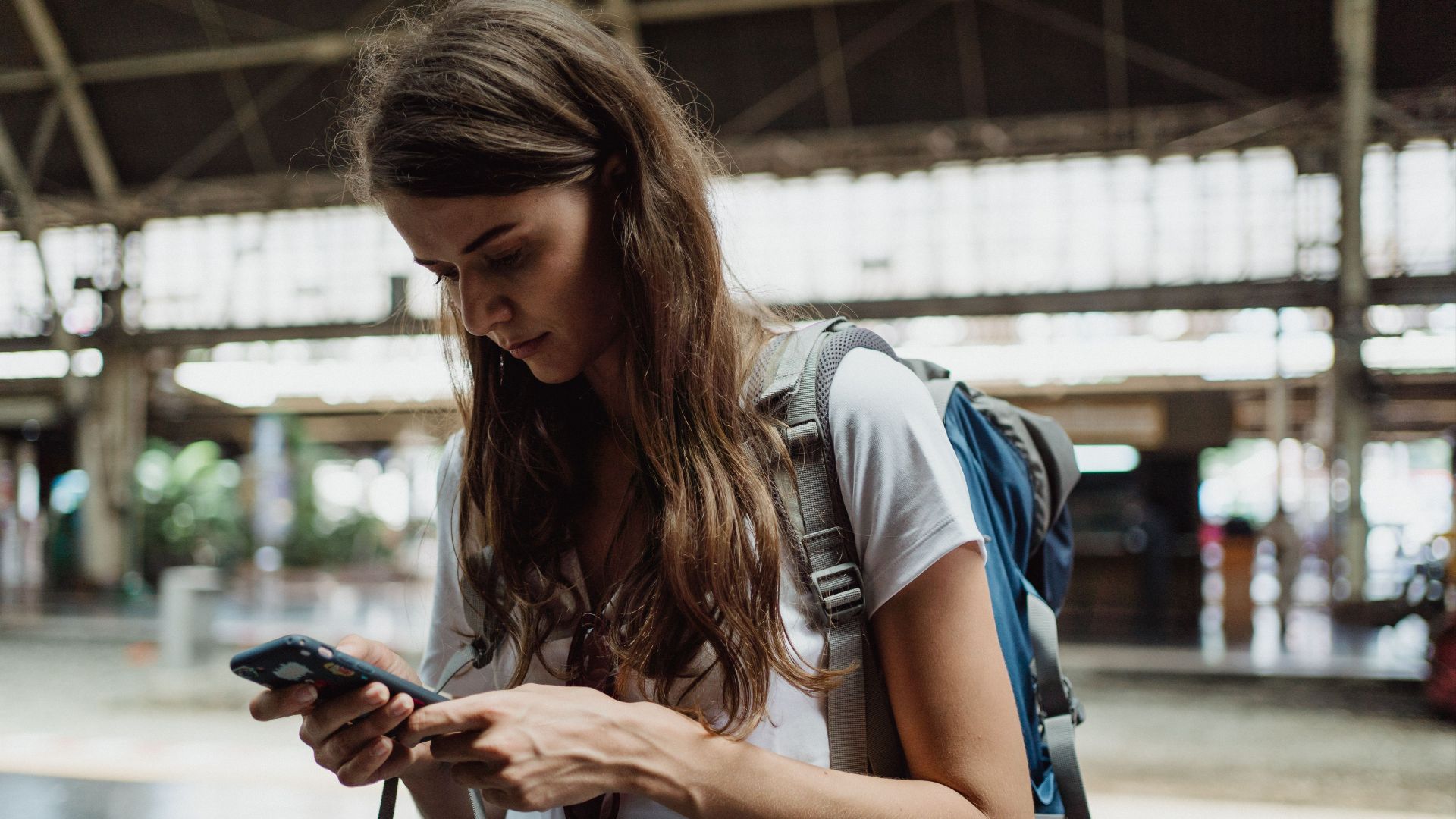 A young woman checks her smartphone while traveling at a train station.