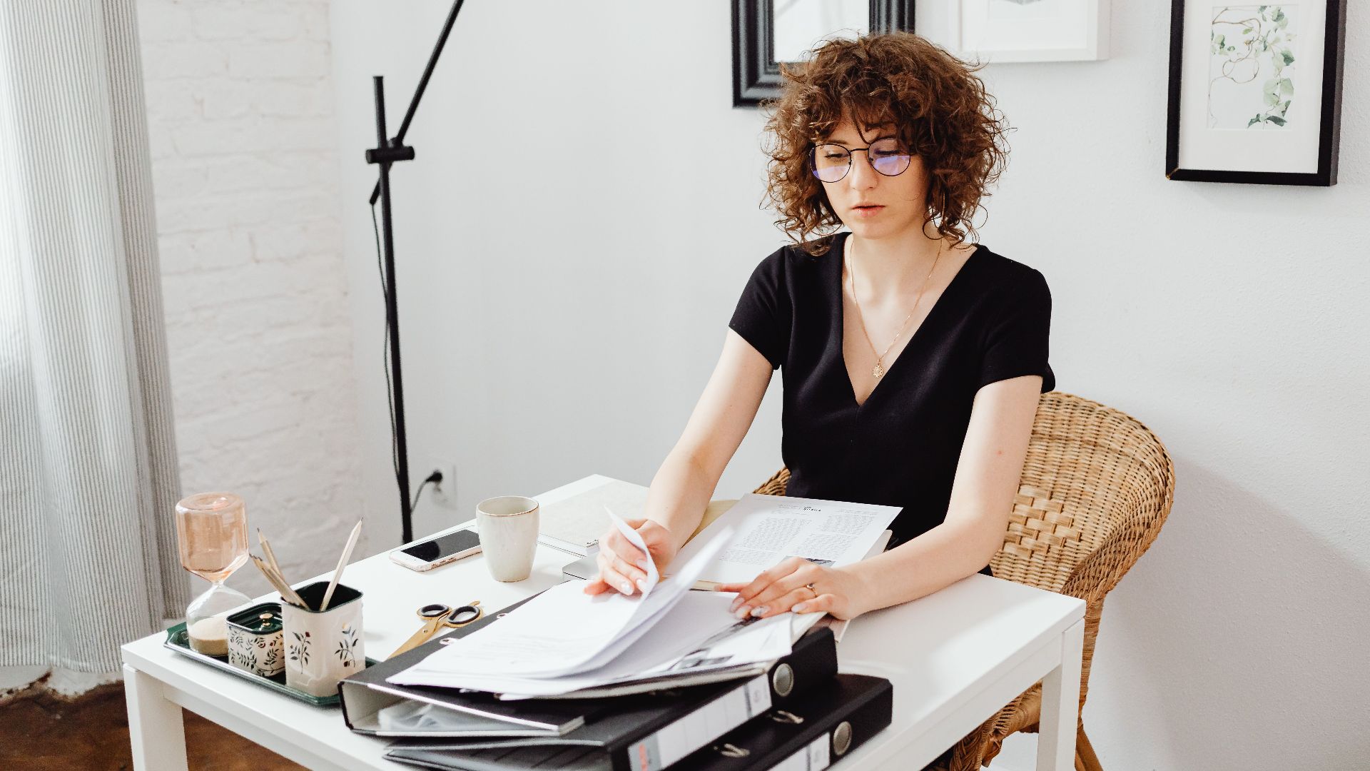 Woman with curly hair and eyeglasses working at a desk in a modern home office.