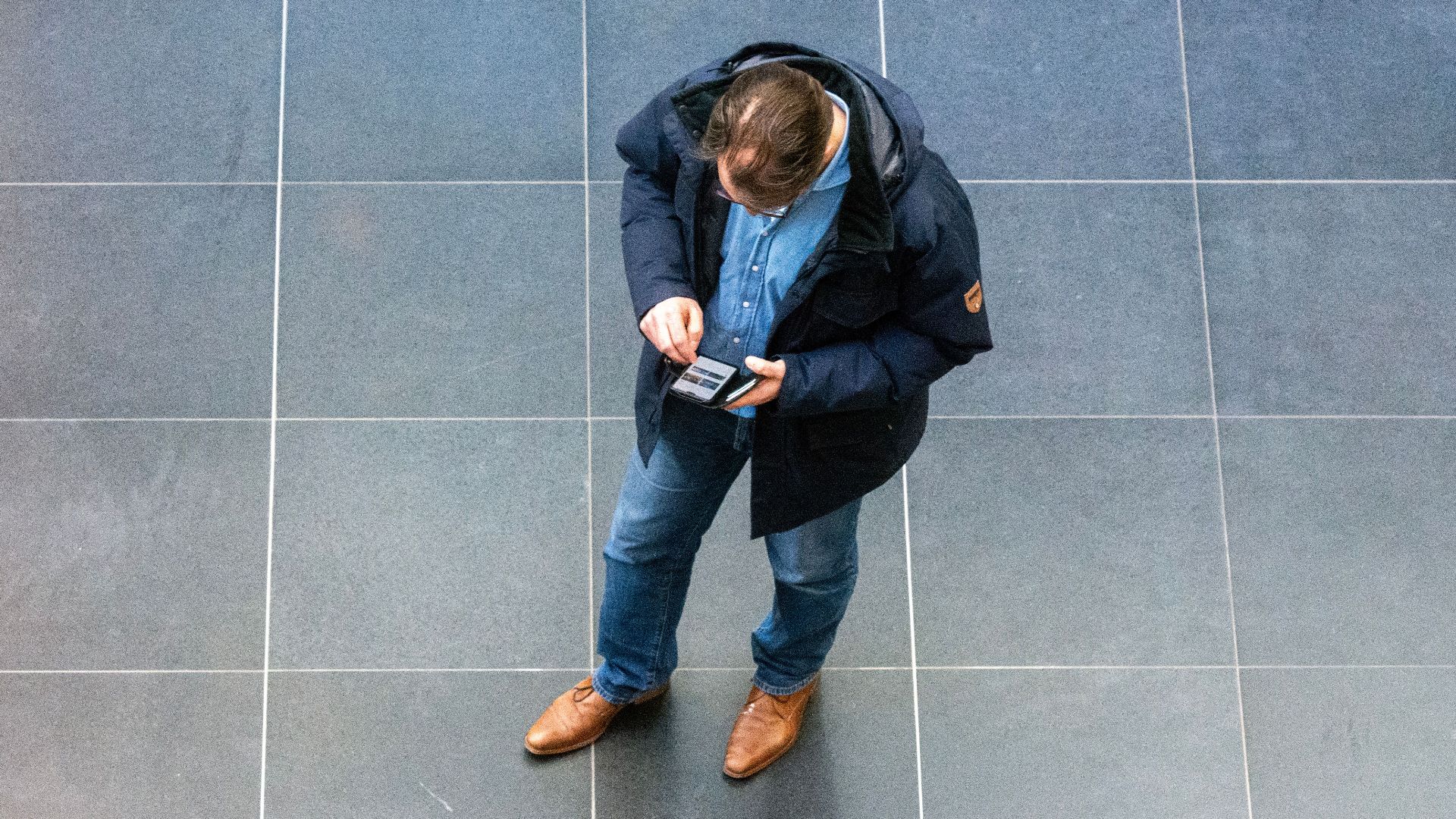 Overhead view of a casually dressed man looking at his phone indoors.