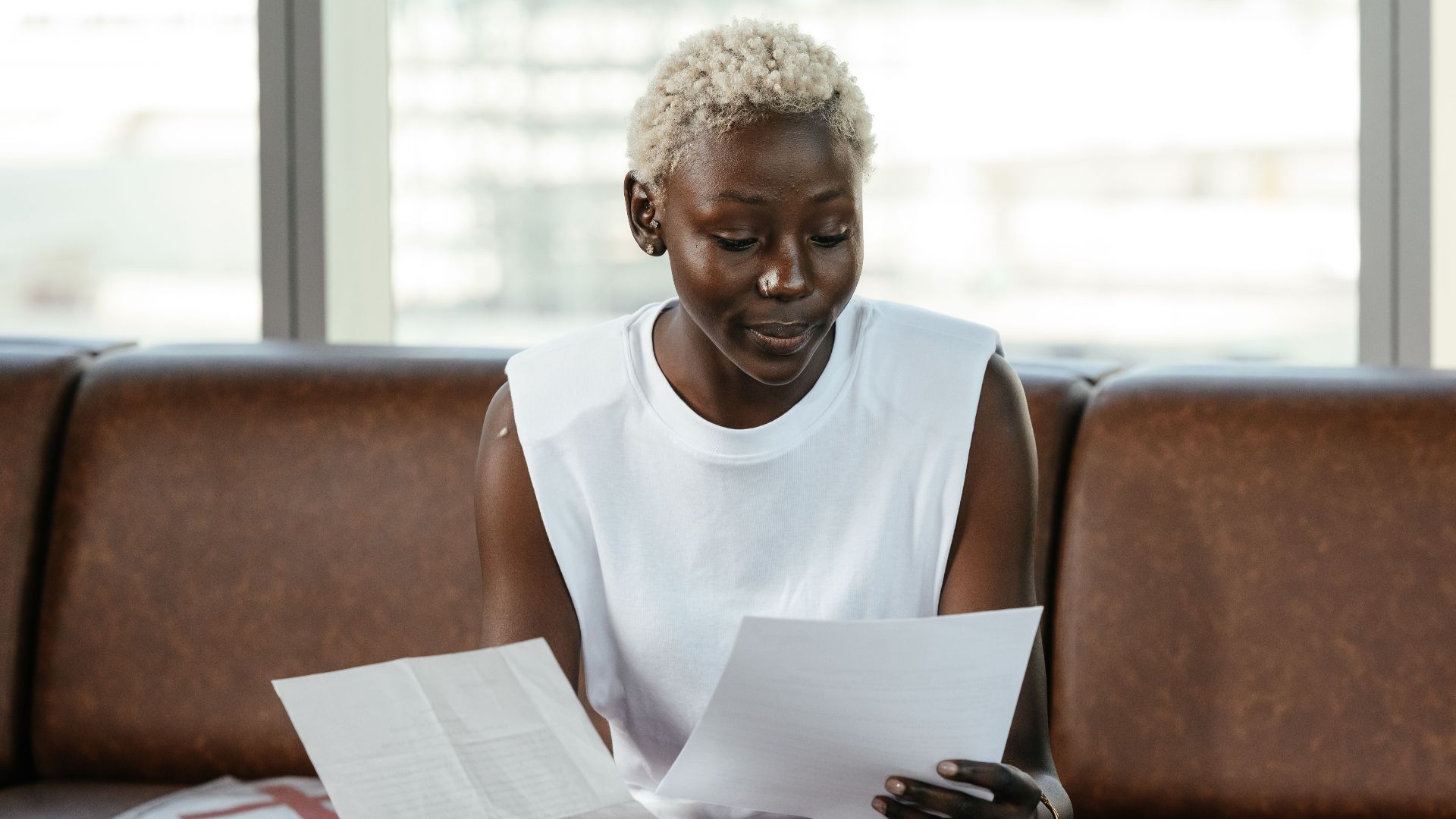 Concentrated African American female comparing important papers of report on leather sofa in office