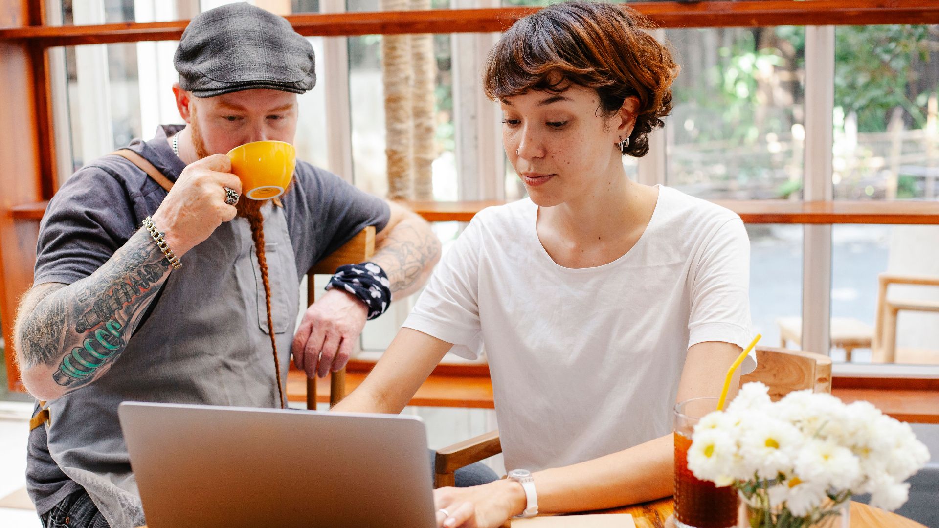 Pensive young woman typing on netbook while man with cup drinking coffee at table of cafe