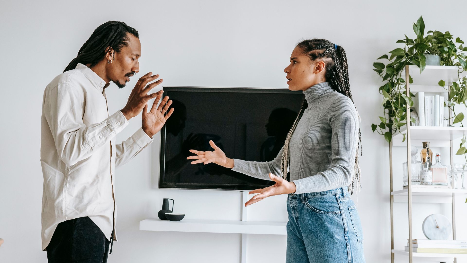 Side view of young African American female in casual outfit gesticulating expressively while arguing with frustrated husband in modern living room