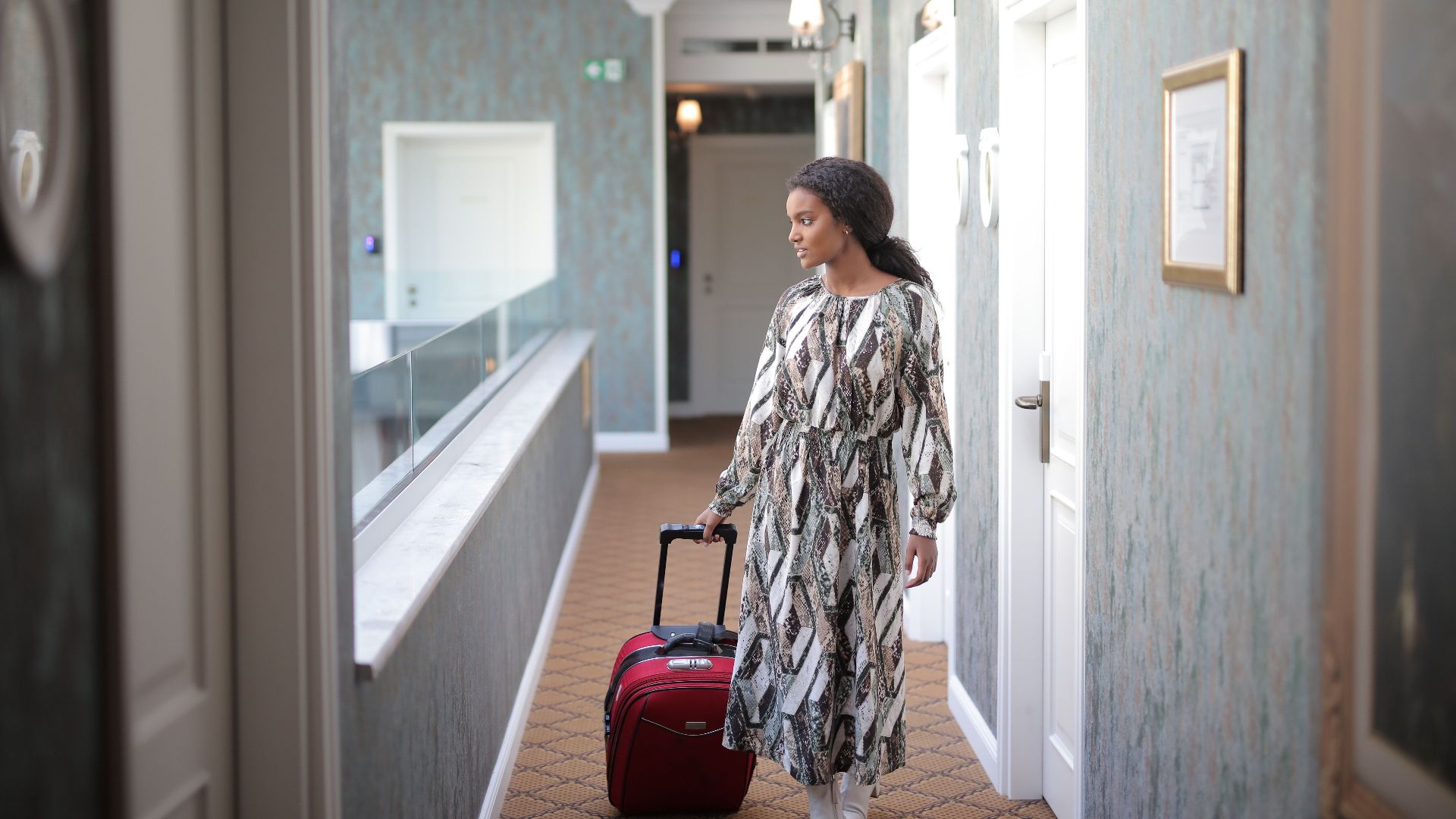 A woman walks with luggage through a stylish hotel corridor, embodying travel elegance.