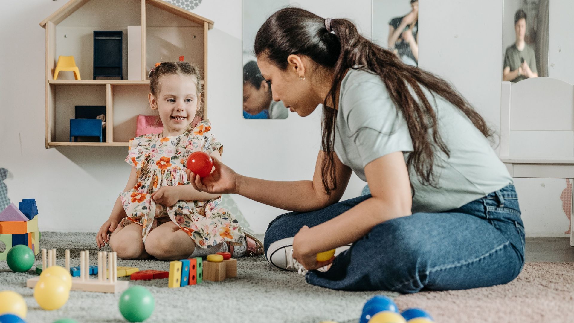 A young girl and woman engaging in an educational play session in a cozy preschool setting.